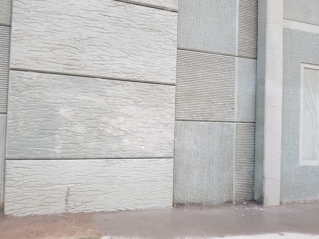 Concrete wall with different textured panels and a smooth sidewalk in front of it.